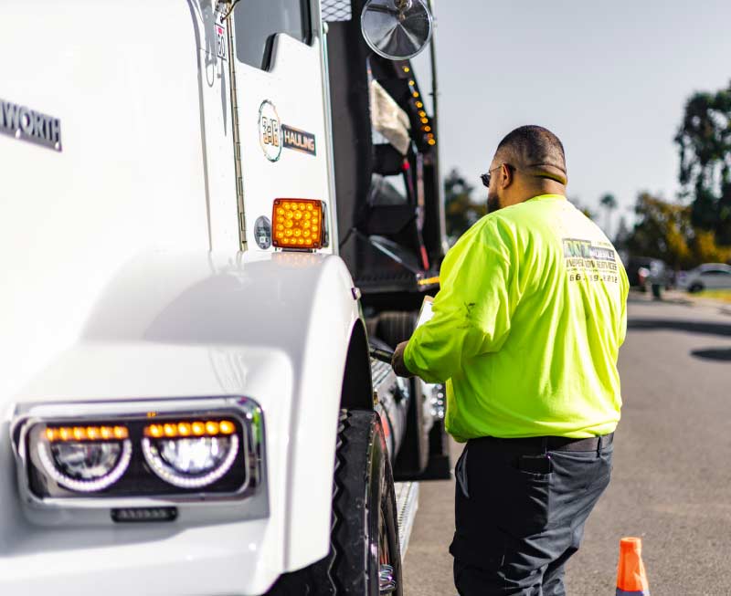 Certified diesel mechanic and inspector conducting a thorough under-the-hood commercial truck inspection at a client's location.